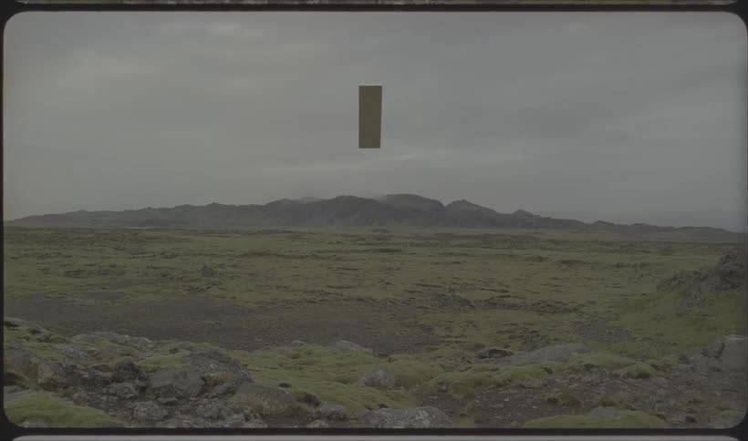 Rectangle rises above field with mountains on the horizon under a cloudy sky