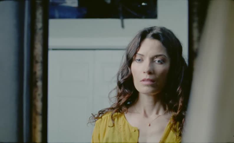 A woman looks at her reflection sighing breathing deep and looking anxious