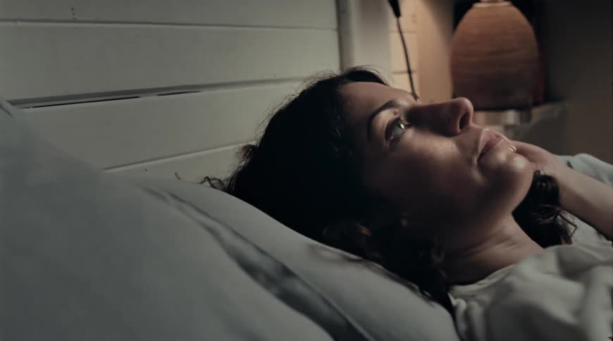 A woman lying in bed flips from her side on to her back and looks up at the ceiling