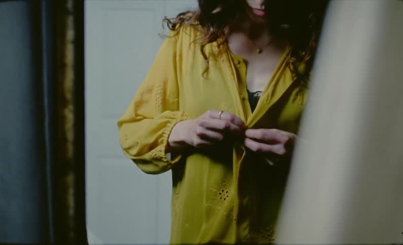 A woman tries to button up a shirt but has problems