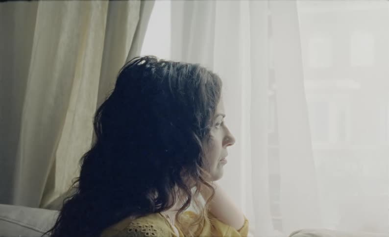 A woman gazing out of a window will sitting on a sofa