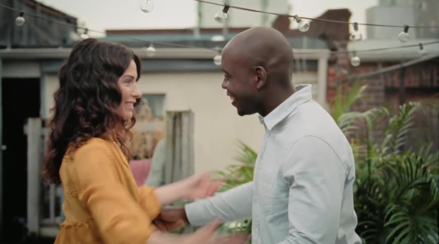 A woman walks up to greet a man she is meeting and she goes in for the hug while he holds out his hand