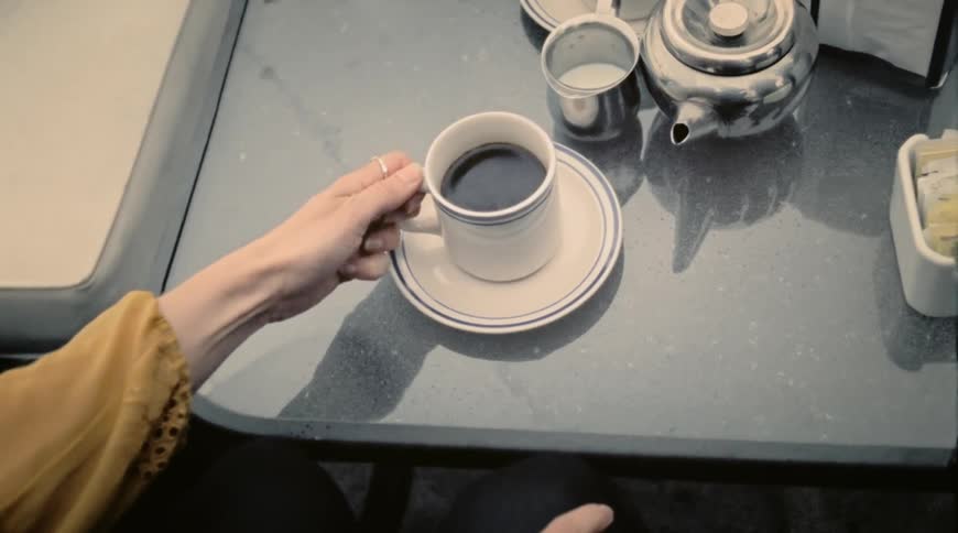 Woman shakily lifts coffee cup needing both hands to stabilize