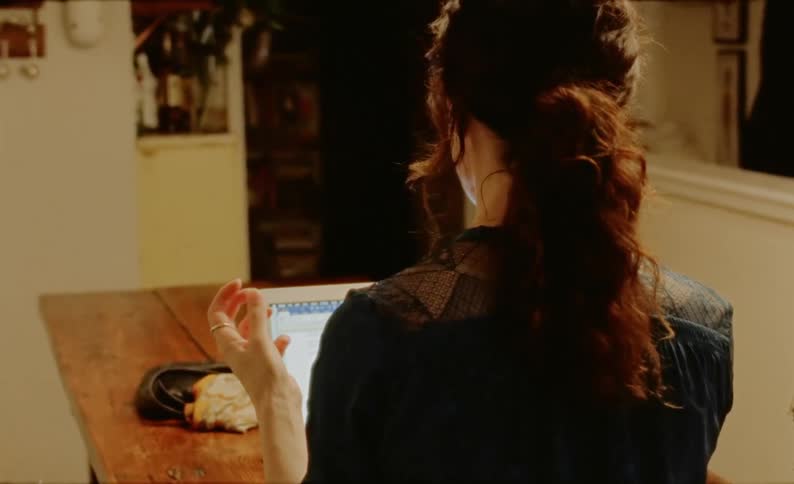A woman sits at a table and uses her laptop while counting on her fingers and clenching her hand