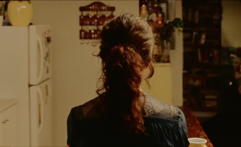The back of a woman at a kitchen table alone with a coffee cup appearing to shiver and sigh