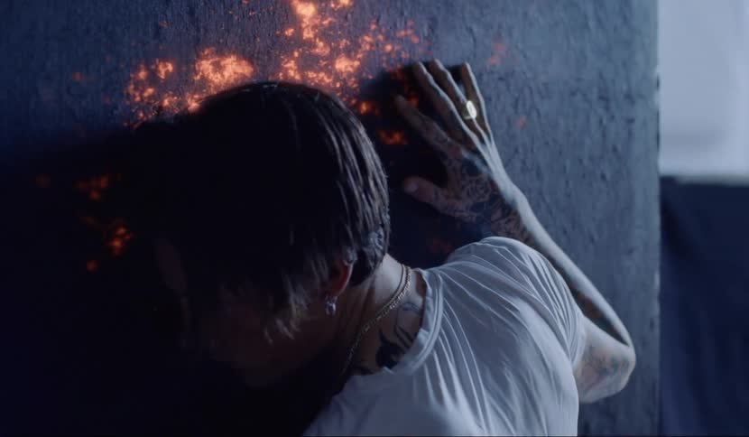 A teenager is up against a black wall that appears to burn orange