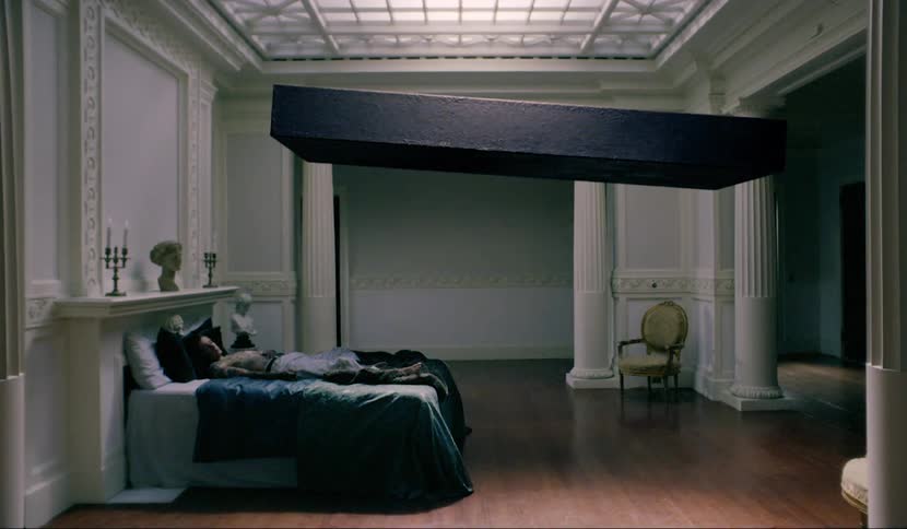 A big wood box floats over a bed that a teen is sleeping in