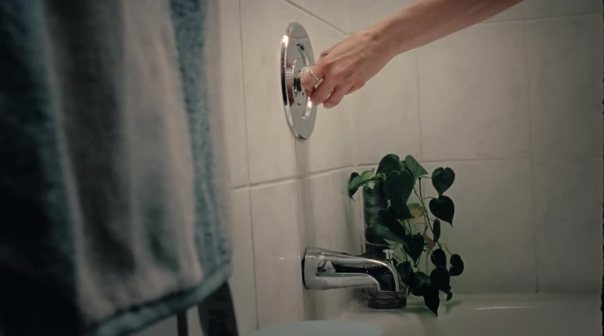 A person with trembling hands turning a handle to turn on the bath faucet
