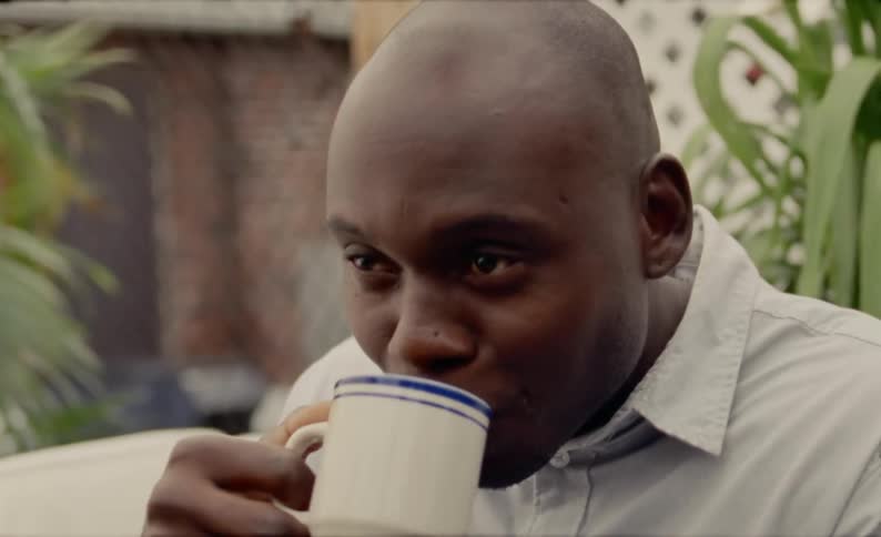 A black man smiles and laughs as he drinks a cup of coffee