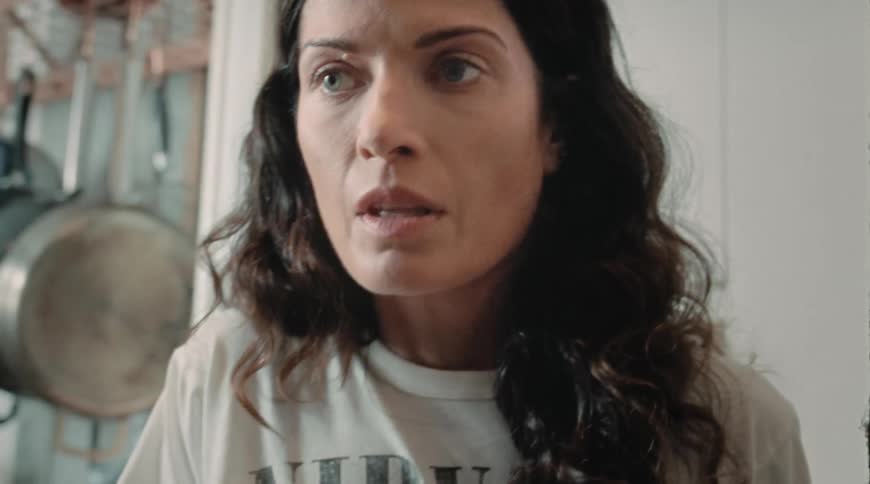 A woman stands in her kitchen and looks nervous