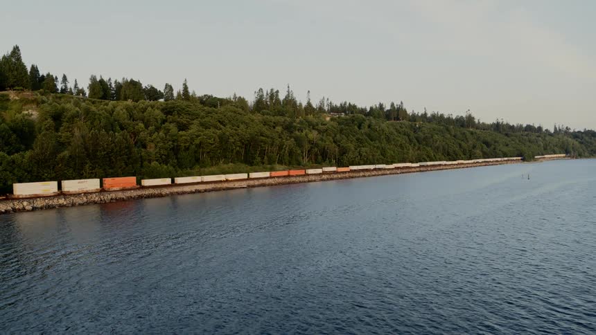 Intermodal container train moving on tracks next to coastal water