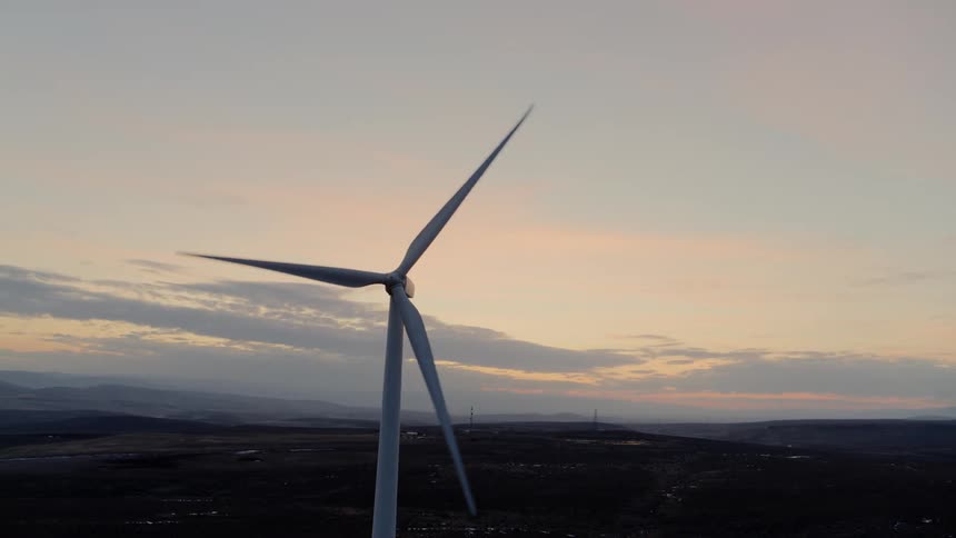 Medium shot of wind turbines spinning against a colorful background sky