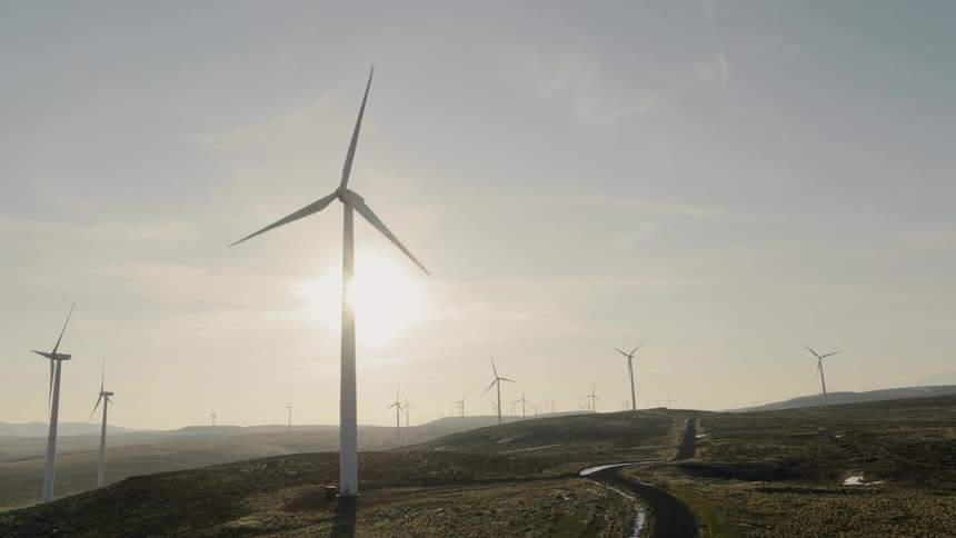 Low angle orbit of a backlit wind turbine surrounded by many others on a wind farm