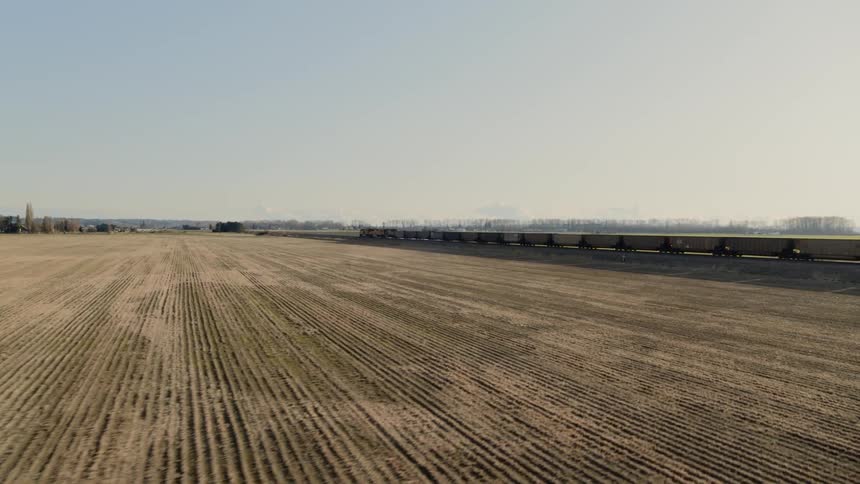 Intersecting a fast moving freight train rolling thru farm fields in a rural area