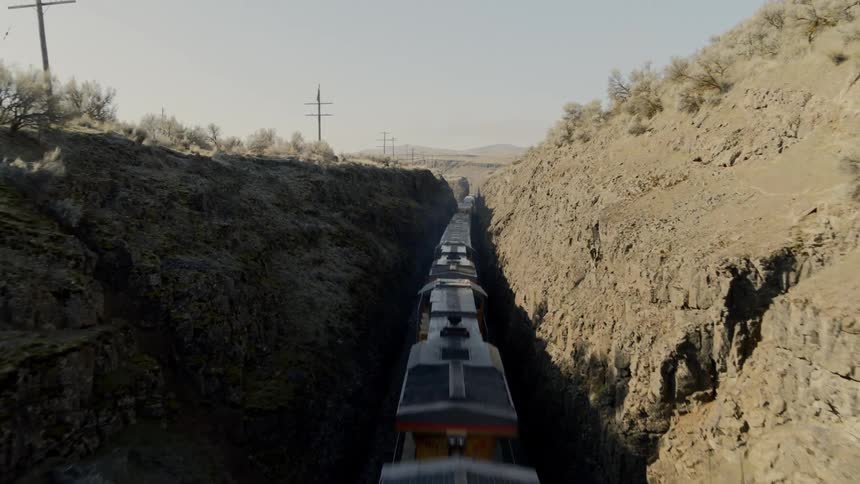 Flyover of a freight train traveling along track in narrow slot canyon