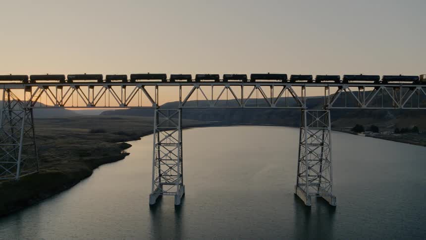 Parallel traverse of tank cars rolling over a railroad trestle bridge