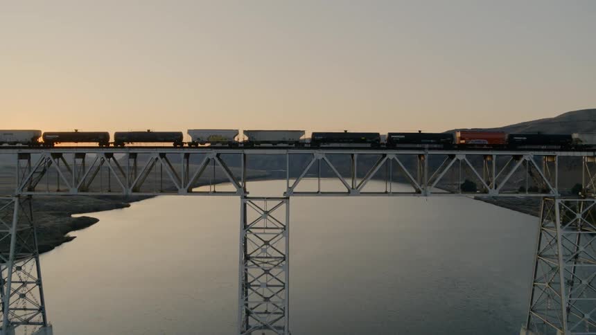 Flying over a freight train crossing a bridge to reveal a beautiful river valley below
