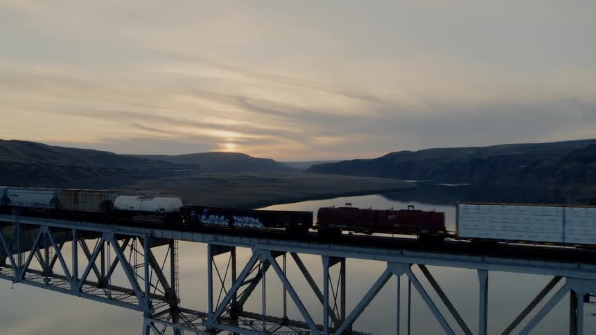 Pullback reveal of a freight train on a high bridge traveling across a river
