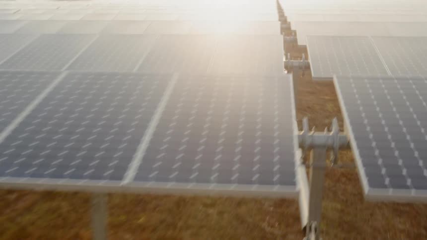 Dynamic low altitude orbit around rows of solar panels as sunlight glints off their surface