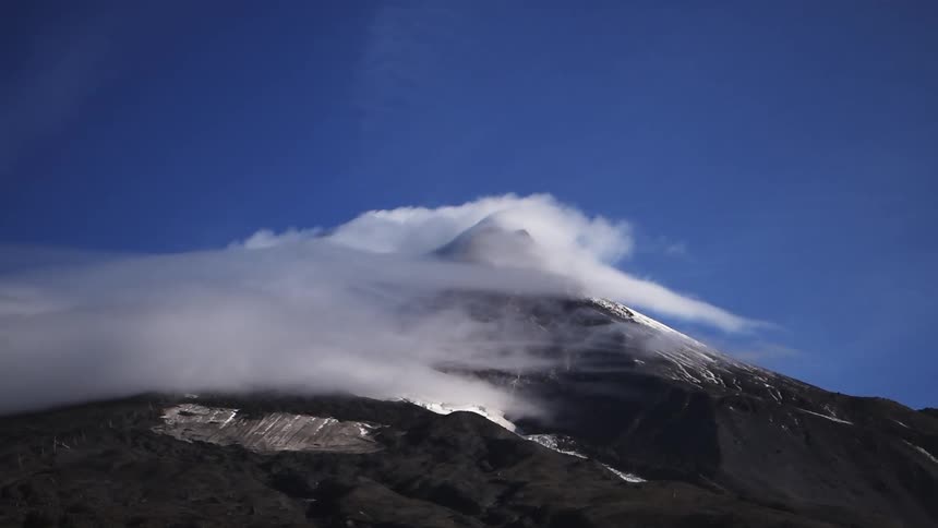 Thin white clouds shown in slow motion rolling over a mountain peak