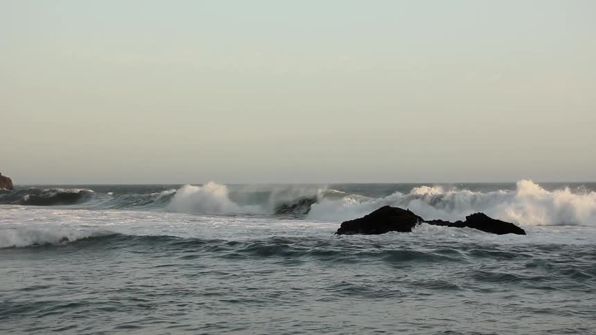 Waves crash on rocks near the shore at dusk