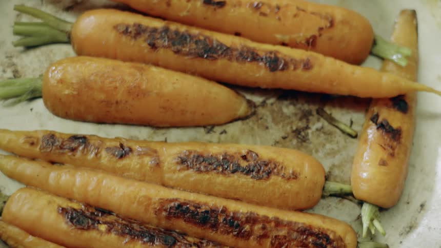 Grilled carrots resting in pan still have part of their tops on