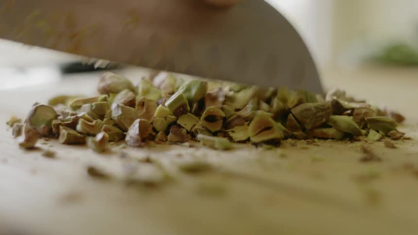 A persons hand chopping nuts with a knife on a cutting board