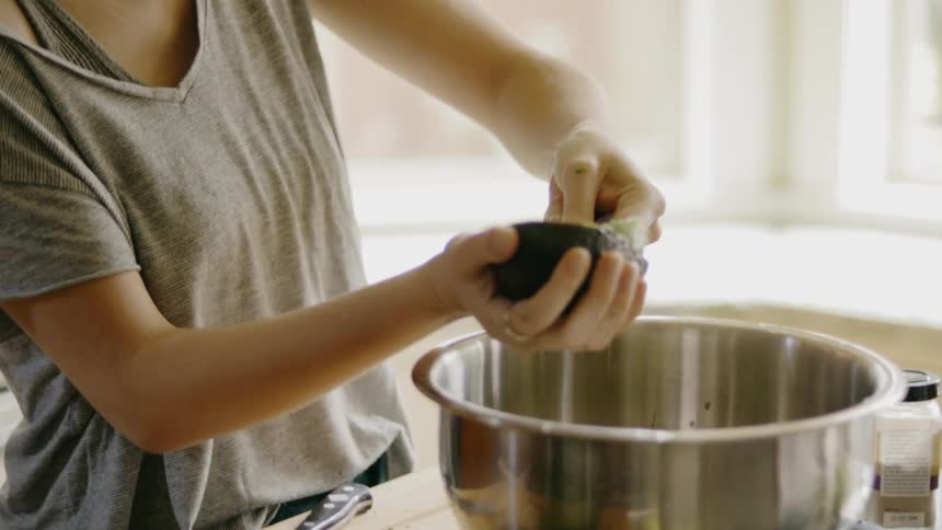 A woman scrapes an avocado in to a bowl
