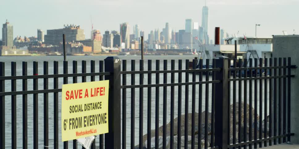 Sign on fence at shoreline across from city advises people to social distance