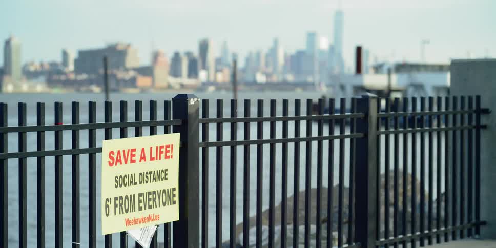 A signed about social distancing in front of a metal fence blocking off a body of water