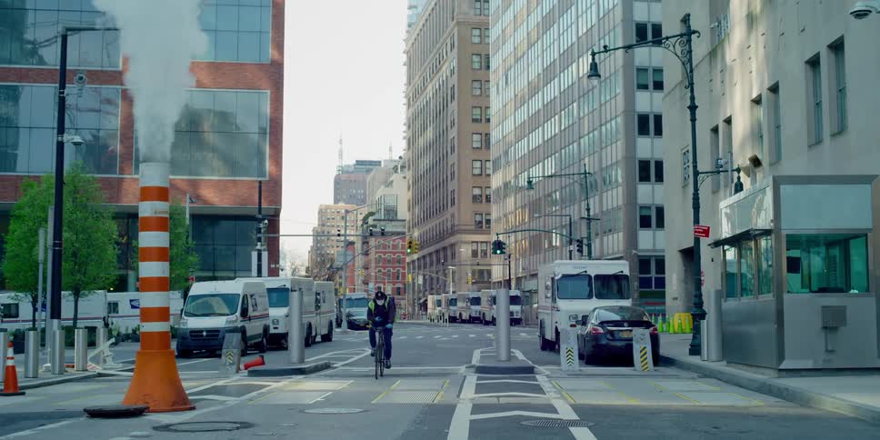 A person rides a bike on a street lined with mail trucks