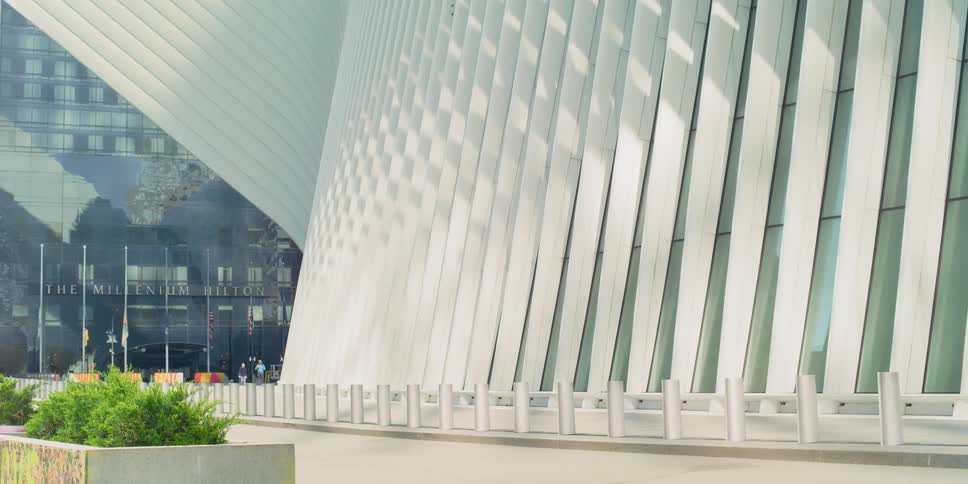 Only a few people walk in front of the millenium hilton in new york near the oculus transportation hub on a sunny day