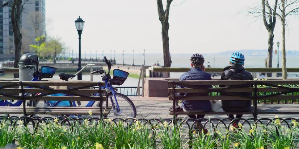 People walk and jog along the water as others sit on a bench after biking