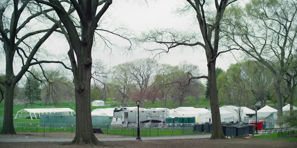 White hospital tents set up in a city park while some people walk on the paths behind