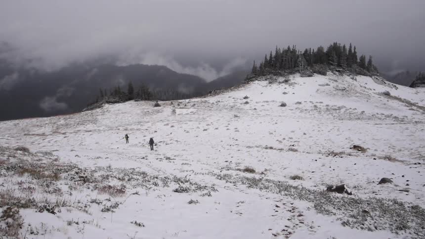 Two people walk on a snow covered mountain plain