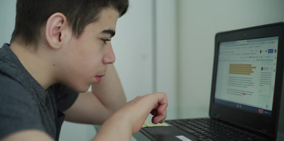A boy sits looking at his laptop screen and word document