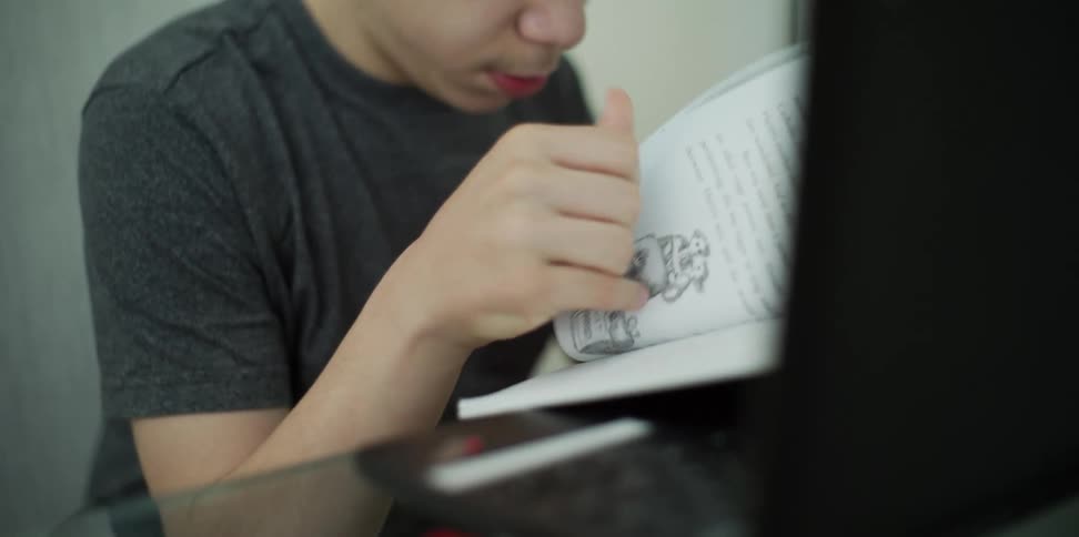 Boy sitting at the desk leafs through a book in his room