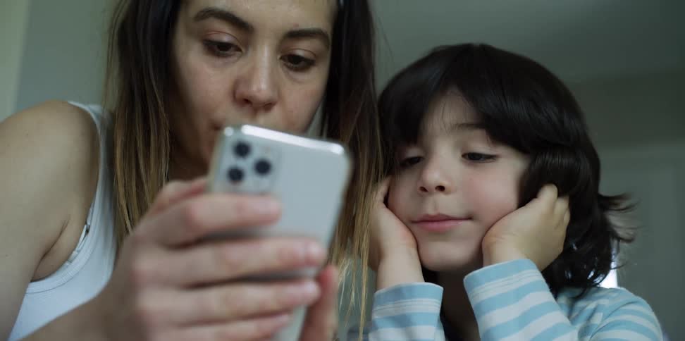 A woman using a smart phone as a boy looks along