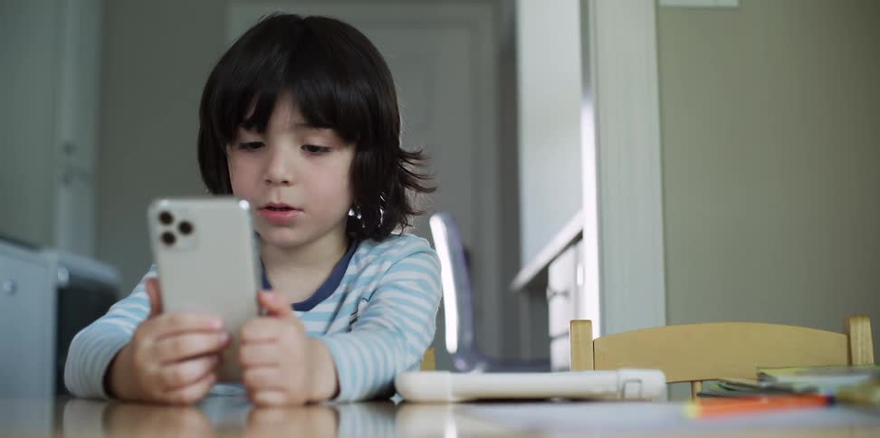 A boy sits at a table and stares at the screen of a smartphone