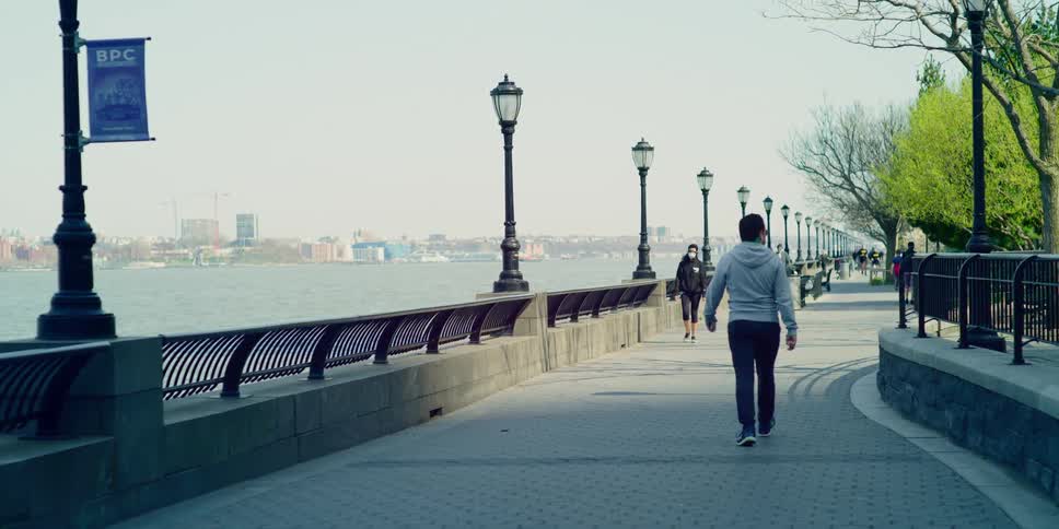 People walk and jog along path paralleling river across from city
