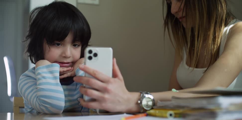 A woman holds her cell phone in front of her son as he smiles
