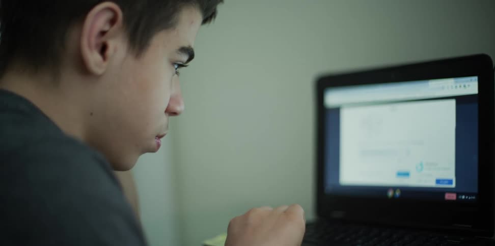 Boy sitting at the desk uses a laptop in his room