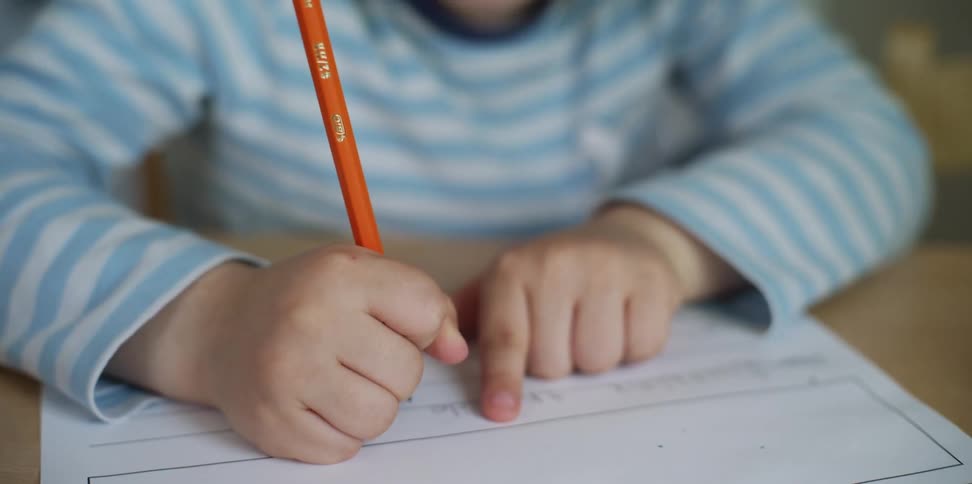 A young boy holds a pencil as he works on homework at a table