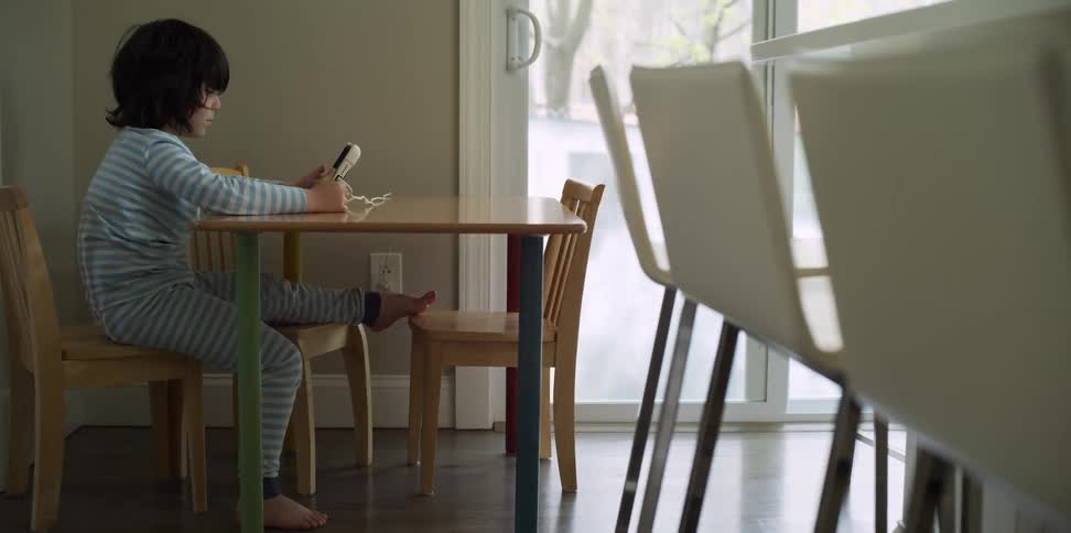 Boy sits at child scale table watching a mobile phone screen