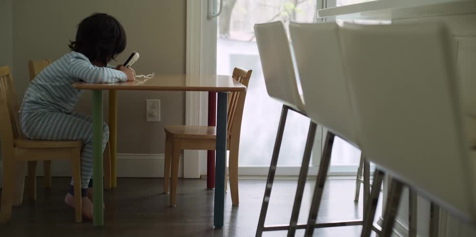 A child sits at a small table watching a smartphone
