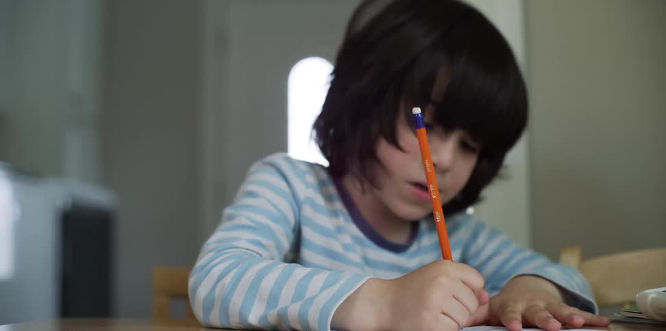 Boy sits at table writing on paper with pencil