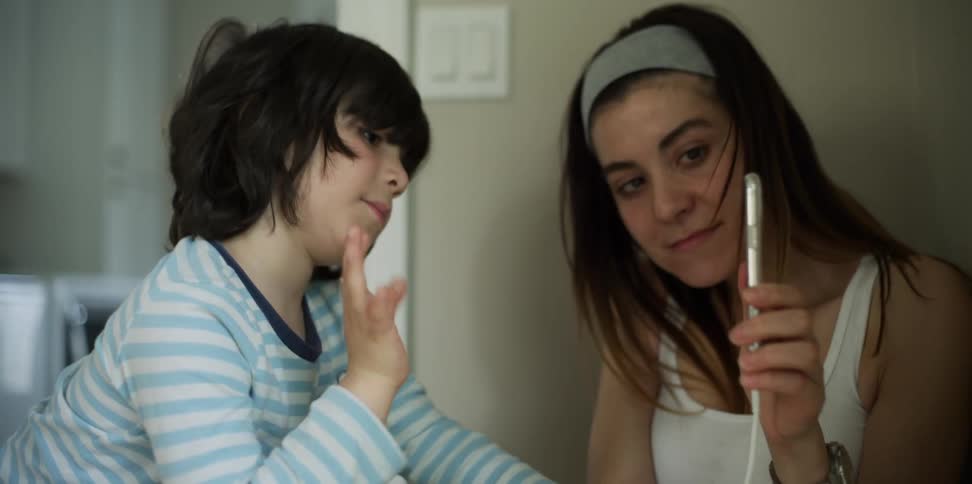 A teenager lets a young boy wave to someone on her cell phone