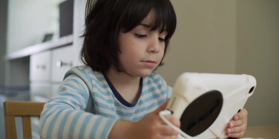 Boy sitting on chair inside house uses tablet for reading