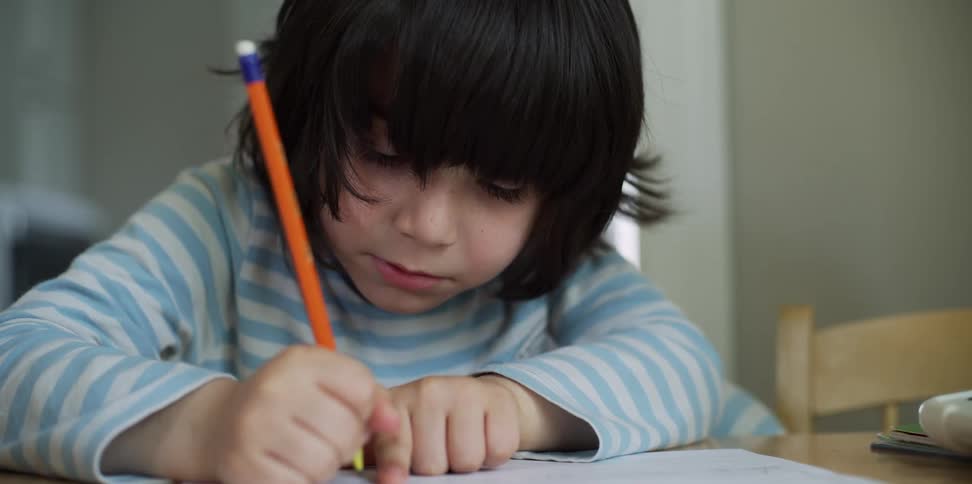 Boy uses paper and pencil to do homework in his home