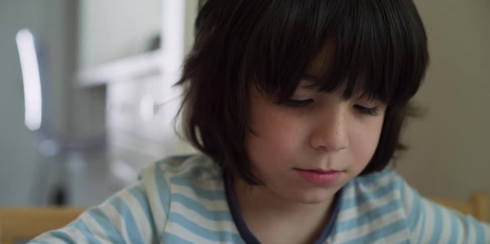 Boy sitting at the desk looks down in his room